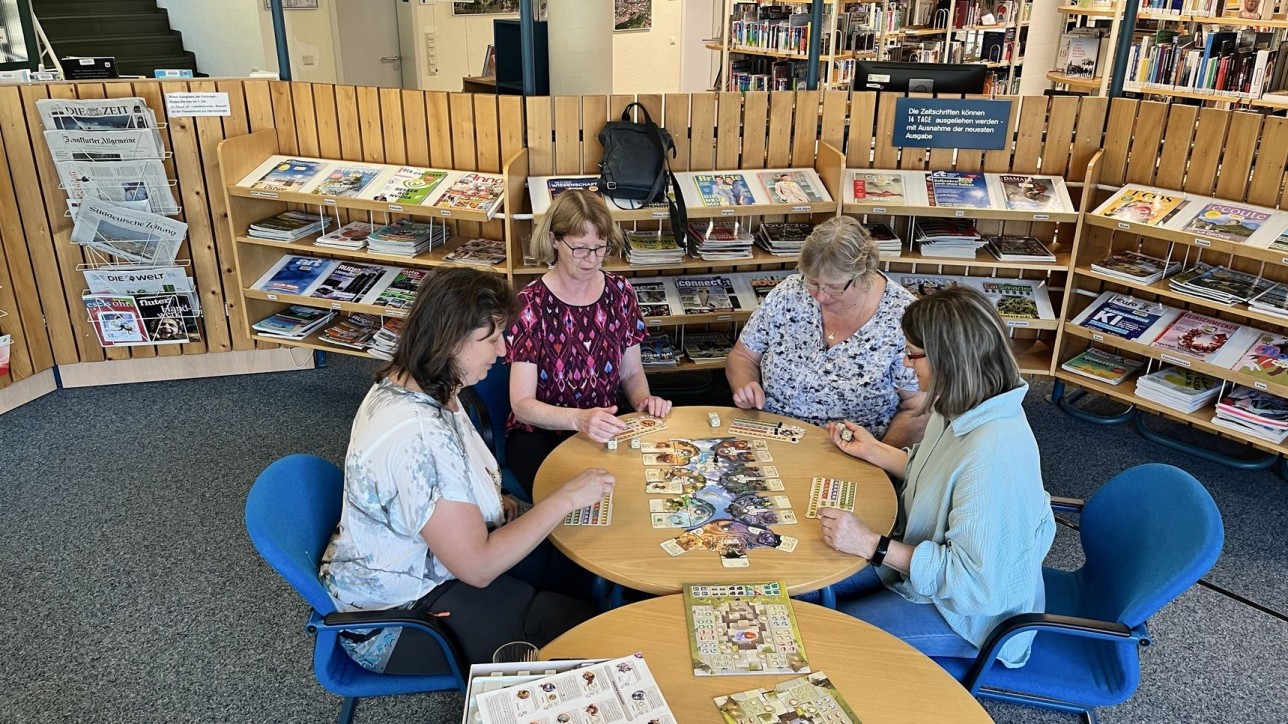 Beim Spieleabend in der Stadtbibliothek Rastatt können Jugendliche und Erwachsene verschiedene Brett- und Kartenspiele ausprobieren. Foto: Olaf Kiesle Menschen sitzen am Tisch und spielen
