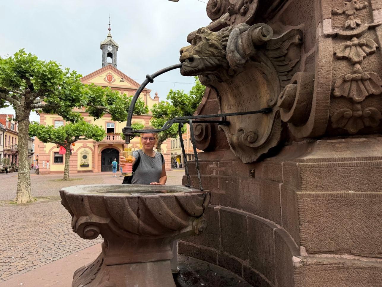An heißen Tagen ist es besonders wichtig, viel Wasser zu trinken. Wo es kostenlose Trinkwasserangebote gibt, zeigt die digitale Hitzekarte auf der städtischen Homepage. Foto: Stadt Rastatt/Isabelle Joyon. Frau füllt Trinkflasche an Trinkbrunnen auf